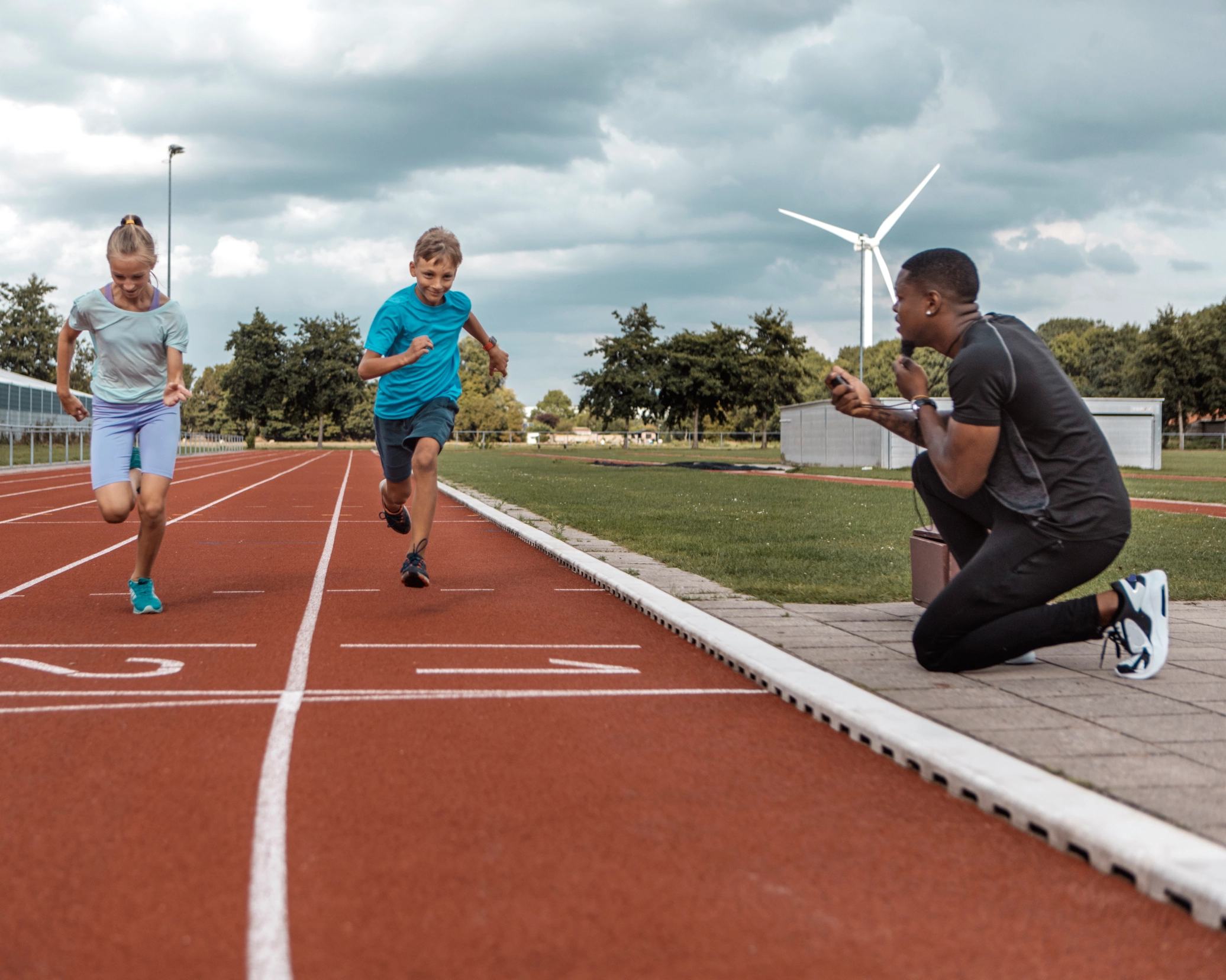 Children running on track with coach timing