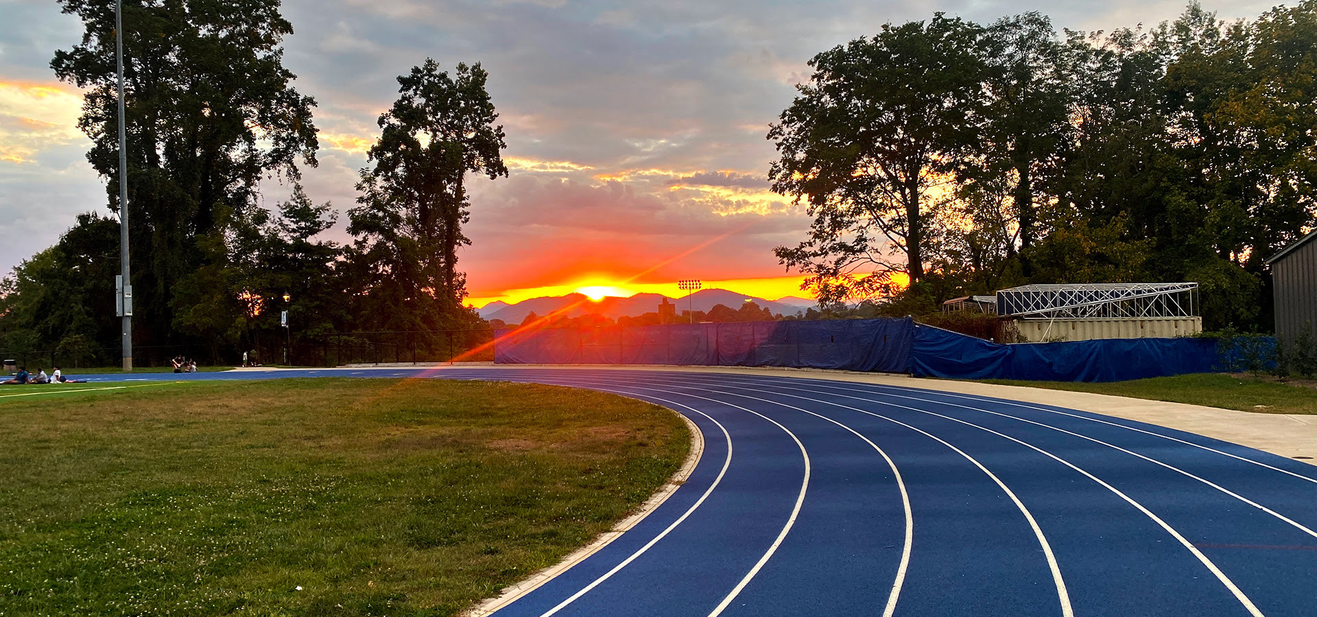 Sunset over blue running track and trees.