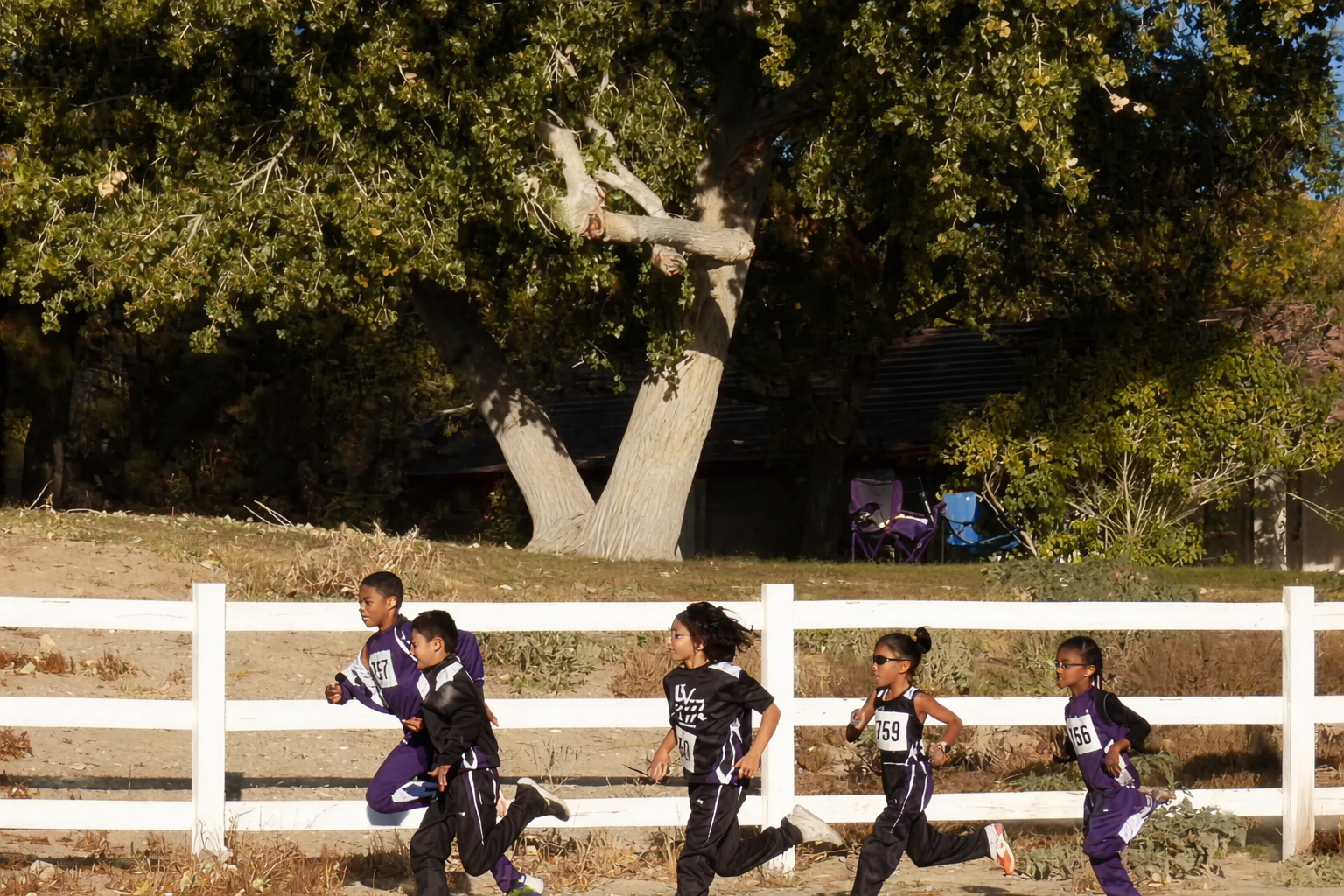 Children running cross-country race by white fence